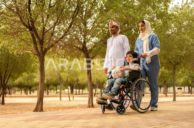 الاستعداد للعب بكرة القدم، ممرضة عربية خليجية عمانية محجبة تقوم بمساعدة ولد يجلس على الكرسي المتحرك، نمط الحياة في سلطنة عمان، رعاية ذوي الاحتياجات الخاصة، تأمين ادوات تساعد أصحاب الهمم على التنقل، أب يستمتع بالتنزه في إحدى الحدائق في الأجواء الصيفية مع ابنه