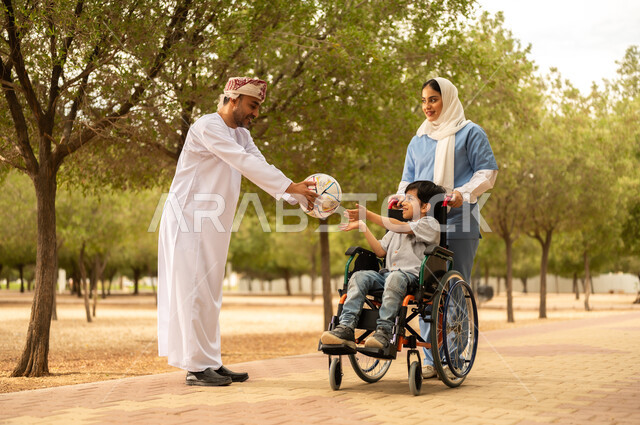 الاستعداد للعب بكرة القدم، ممرضة عربية خليجية عمانية محجبة تقوم بمساعدة ولد يجلس على الكرسي المتحرك، نمط الحياة في سلطنة عمان، رعاية ذوي الاحتياجات الخاصة، تأمين ادوات تساعد أصحاب الهمم على التنقل، أب يستمتع بالتنزه في إحدى الحدائق في الأجواء الصيفية مع ابنه