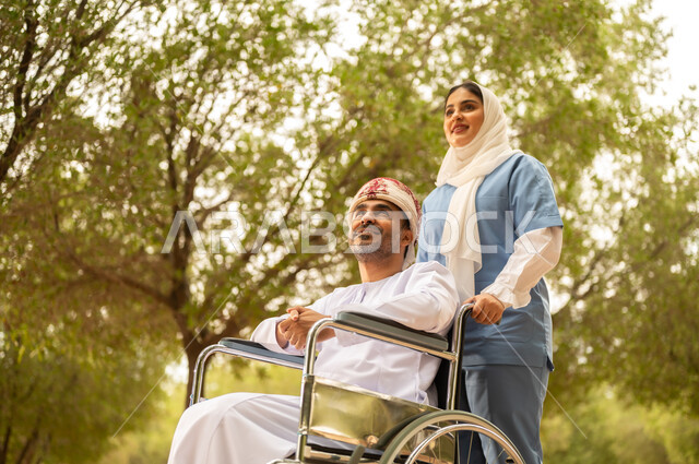 تأمين ادوات تساعد أصحاب الهمم على التنقل والحركة، الاستمتاع  بالأجواء الصيفيه المشمسة، التنزه في احدى الحدائق، ممرضة عربية خليجية عمانية محجبة تقوم بمساعدة رجل يرتدي الدشداشة والعمامة يجلس على الكرسي المتحرك، الرعاية والاهتمام بذوي الاحتياجات
