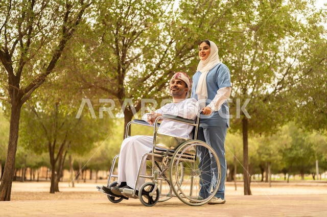 الرعاية والاهتمام بذوي الاحتياجات، تأمين ادوات تساعد أصحاب الهمم على التنقل والحركة، الاستمتاع  بالأجواء الصيفيه المشمسة، التنزه في احدى الحدائق، ممرضة عربية خليجية عمانية محجبة تقوم بمساعدة رجل يرتدي الدشداشة والعمامة يجلس على الكرسي المتحرك