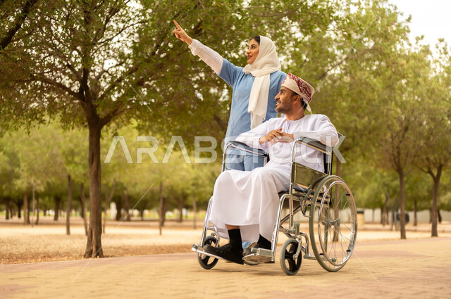 Caring for and paying attention to people with special needs, providing tools to help people with disabilities move around, enjoying the sunny summer weather, taking a walk in a park, a veiled Gulf Arab Omani nurse helping a man wearing a dishdasha and turban sitting in a wheelchair