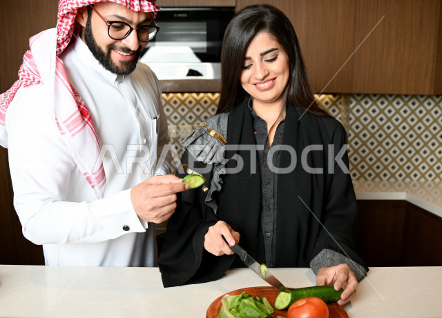 زوجان عربيان خليجيان سعوديان يساعدان بعضهم في اعداد وتجهيز الطعام ، تقطيع الخضراوات لاعداد السلطة الشهية ، تحضير وجبة صحية