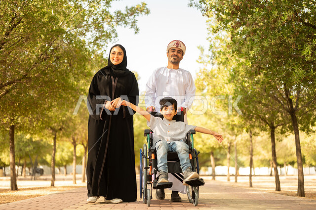 ولد عماني مقعد يجلس على كرسي متحرك في أحد المنتزهات، منح مرضى ذوي الإعاقة الحركية طاقة ايجابية، شعور ذوي الهمم بالراحه والطمأنينه في بيئتهم، عائلة عربيه خليجيه عمانية برفقه ابنها في إحدى الحدائق للاستمتاع بالهواء الطلق