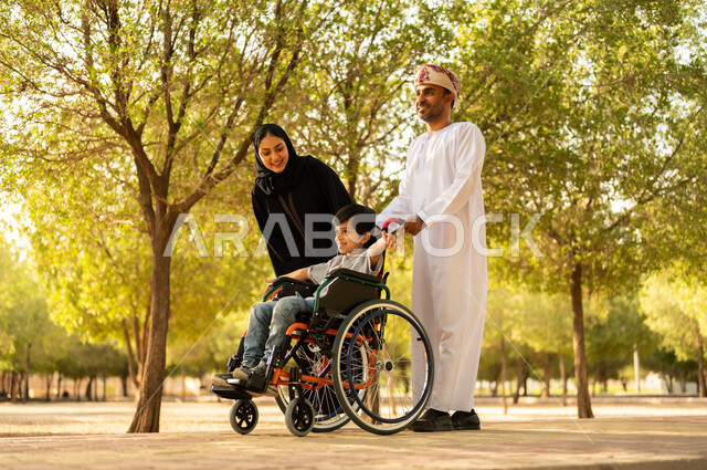 ولد عماني مقعد يجلس على كرسي متحرك في أحد المنتزهات، منح مرضى ذوي الإعاقة الحركية طاقة ايجابية، شعور ذوي الهمم بالراحه والطمأنينه في بيئتهم، عائلة عربيه خليجيه عمانية برفقه ابنها في إحدى الحدائق للاستمتاع بالهواء الطلق