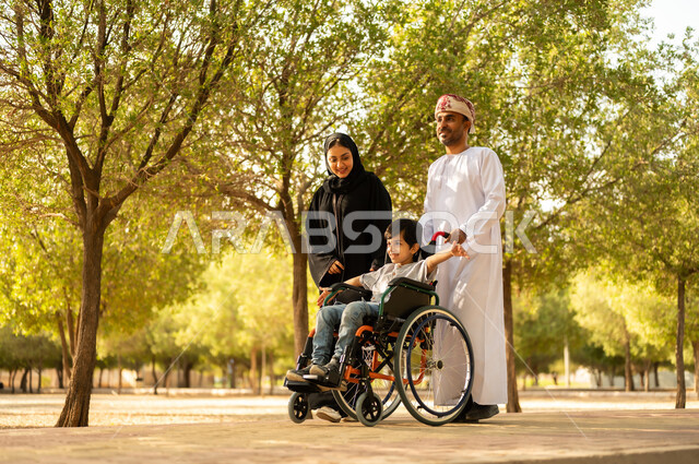 ولد عماني مقعد يجلس على كرسي متحرك في أحد المنتزهات، منح مرضى ذوي الإعاقة الحركية طاقة ايجابية، شعور ذوي الهمم بالراحه والطمأنينه في بيئتهم، عائلة عربيه خليجيه عمانية برفقه ابنها في إحدى الحدائق للاستمتاع بالهواء الطلق