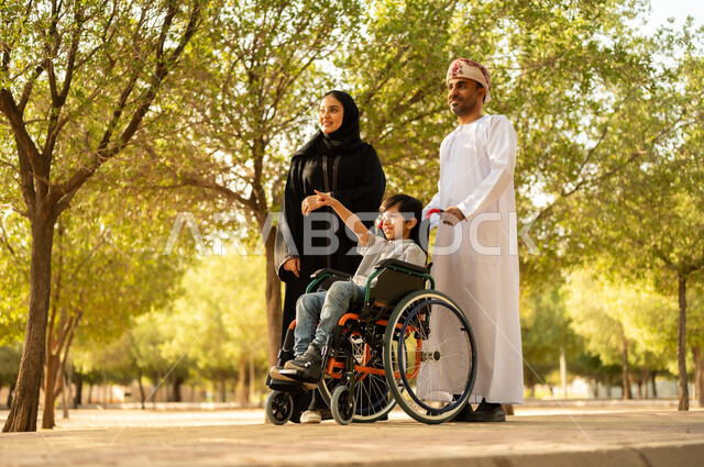 ولد عماني مقعد يجلس على كرسي متحرك في أحد المنتزهات، منح مرضى ذوي الإعاقة الحركية طاقة ايجابية، شعور ذوي الهمم بالراحه والطمأنينه في بيئتهم، عائلة عربيه خليجيه عمانية برفقه ابنها في إحدى الحدائق للاستمتاع بالهواء الطلق