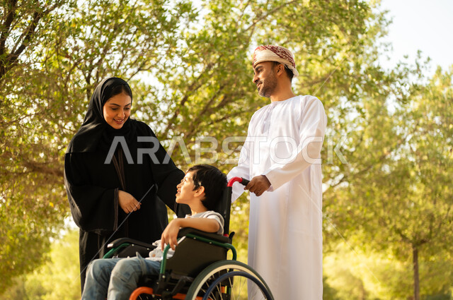 ولد عماني مقعد يجلس على كرسي متحرك في أحد المنتزهات، منح مرضى ذوي الإعاقة الحركية طاقة ايجابية، شعور ذوي الهمم بالراحه والطمأنينه في بيئتهم، عائلة عربيه خليجيه عمانية برفقه ابنها في إحدى الحدائق للاستمتاع بالهواء الطلق