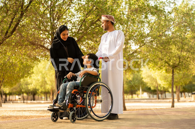 منح مرضى ذوي الإعاقة الحركية طاقة ايجابية، شعور ذوي الهمم بالراحه والطمأنينه في بيئتهم, عائلة عربيه خليجيه عمانية برفقه ابنها في إحدى الحدائق للاستمتاع بالهواء الطلق، ولد عامني مقعد يجلس على كرسي متحرك في أحد المنتزهات