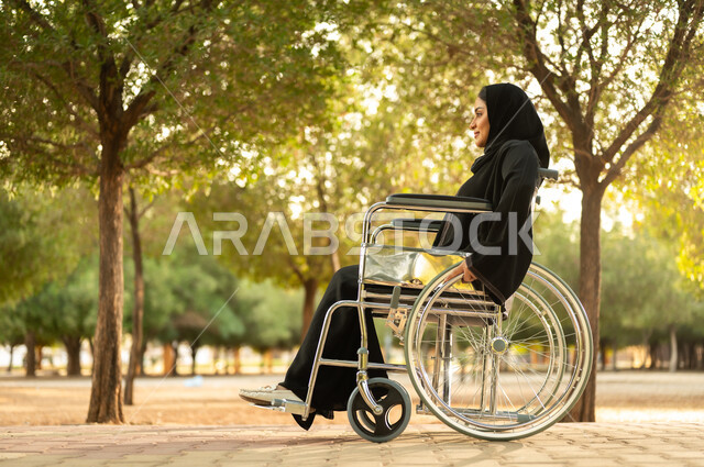 توفير اجهزة ومعدات تساعد بالحركة والتنقل، سيدة سعودية من ذوي الاحتياجات الخاصه تقضي وقت ممتع في الحديقة، شعور المعاقين بالإنتماء والتقدير، إمرأة مقعدة عربية خليجية عمانية ترتدي الحجاب والعباءة تجلس على كرسي متحرك في احدى المنتزهات