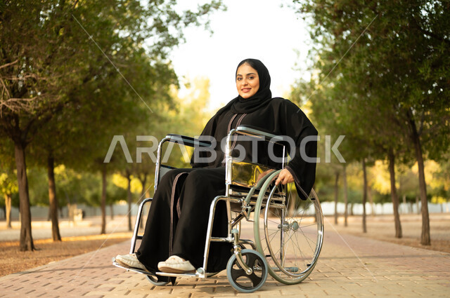 Providing devices and equipment to aid movement and mobility, a Saudi woman with special needs spending a pleasant time in the park, the sense of belonging and appreciation for the disabled, a disabled Arab Gulf Omani woman wearing a hijab and abaya sitting in a wheelchair in a park