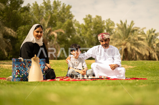 الجلوس في الطبيعة الخضراء، مفهوم التحدي والتركيز، عائلة عربية خليجية عمانية تقضي أوقات ممتعة في إحدى الحدائق في سلطنة عمان، أنشطة عائلية في الأجواء الصيفية، نزهه في الهواء الطلق، التسلية في لعبة الضامة