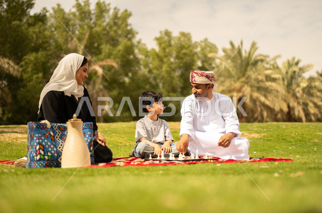 الجلوس في الطبيعة الخضراء، مفهوم التحدي والتركيز، عائلة عربية خليجية عمانية تقضي أوقات ممتعة في إحدى الحدائق في سلطنة عمان، أنشطة عائلية في الأجواء الصيفية، نزهه في الهواء الطلق، التسلية في لعبة الضامة