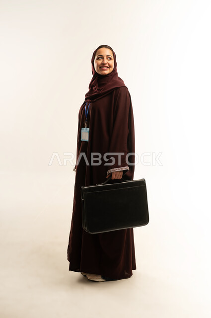 Going to work actively, business and project management concept, portrait of a veiled Omani Gulf Arab woman wearing a brown abaya holding a black bag, a smiling Saudi woman looking at something, elegance and interest in appearance, full body, white background