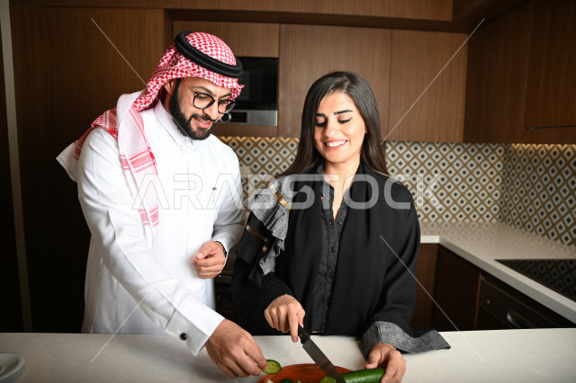 زوجان عربيان خليجيان سعوديان يساعدان بعضهم في اعداد وتجهيز الطعام ، تقطيع الخضراوات لاعداد السلطة الشهية ، تحضير وجبة صحية