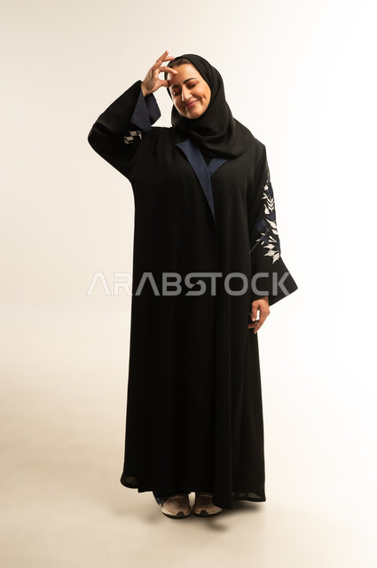 الشعور بالإرهاق وفقدان التركيز, الاحساس بالشقيقية والصداع النصفي, الاجهاد والضغط النفسي, بورتريه لامراه عربيه خليجيه عمانيه ترتدي العباءه السوداء تقوم بوضع  يديها على رأسها، سيده سعودية تغمض عينيها بإيماءات ألم الرأس الشديد, صورة الجسم بالطول الكامل, خلفية بيضاء