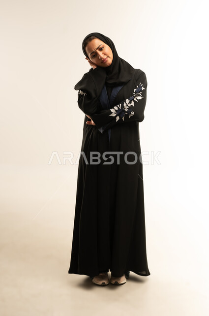 Meditation and planning for the future, a Saudi woman thinking and trying to find a solution to a problem, a portrait of a veiled Gulf Arab Omani woman wearing a black abaya, standing and placing her hand on her cheek with gestures of concentration and contemplation, full-length body, white background