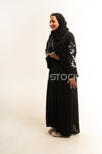 الحاجه الى العلاج، أمراض والتهابات الجهاز الهضمي، سيده سعوديه تعاني من آلام البطن والمعدة، بورتريه لامراة عربيه خليجيه عمانية ترتدي العباءه السوداء  تقوم بوضع يديها على بطنها بتعابير التعب والإرهاق والإحساس بالمرض، الجسم بالطول الكامل، خلفية بيضاء