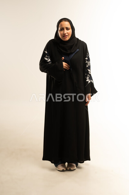 الشعور بحرقة في المعدة وعسر الهضم، الحاجه للمساعدة وطلب العلاج، سيده سعوديه تشعر بالمغص والوجع، بورتريه لامرأه عربيه خليجيه عمانية ترتدي عباءة سوداء تضع يدها على بطنها تنحني من شدة الألم، إيماءات التقيؤ والغثيان، صورة لكامل الجسم، خلفية بيضاء