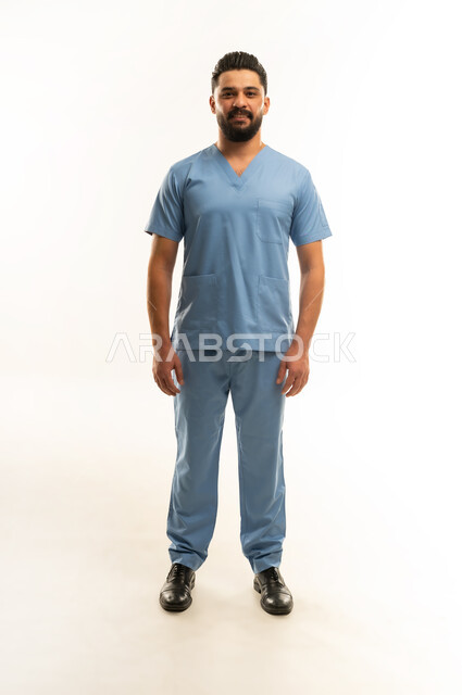 الاستعداد لتقديم الخدمات الطبية للمرضى, مفهوم الطب والرعاية الصحية، ممرض سعودي يعمل بالقطاع الطبي، الوقوف باستعداد والنظر إلى الكاميرا بإيماءات السرور, بورتريه لشاب عربي خليجي عماني مبتسم يرتدي يونيفورم العمليقف باستقامة, الجسم بالطول الكامل، خلفية بيضاء