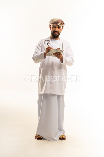 تدوين وتسجيل الوصفة، الفحص الطبي وتقديم الخدمات العلاجية, بورتريه لطبيب عربي خليجي عماني يرتدي الدشداشة والعمامة والمعطف الطبي يضع السماعة الطبية يعمل في  العمل في القطاع الصحي في سلطنة عمان، الجسم بالطول الكامل، خلفية بيضاء