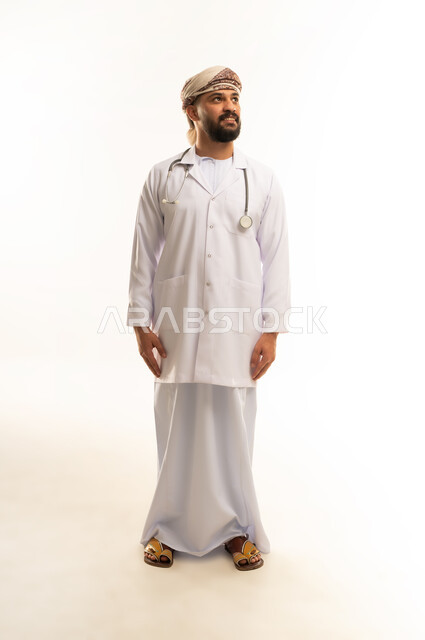 العمل في القطاع الصحي في سلطنة عمان، الفحص الطبي وتقديم الخدمات العلاجية للمرضى, بورتريه لطبيب عربي خليجي عماني يرتدي الدشداشة والعمامة والمعطف الطبي يضع السماعة الطبية يقف باستقامة ينظر إلى شيء ما بإيماءات الثقة بالنفس، الجسم بالطول الكامل، خلفية بيضاء