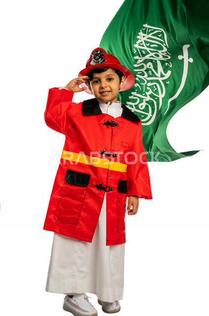 بورتريه لفتى عربي خليجي سعودي أنيق ، يرتدي زي رجل الإطفاء ، يلقي التحية لوطنه الحبيب المملكة العربية السعودية ، خلفه علم المملكة ، اليوم الوطني السعودي ، مفهوم مهنة الدفاع المدني ، المهنة المستقبلية ، خلفية بيضاء ، يرتدي خوذة وسترة الحماية الخاصة بالعمل