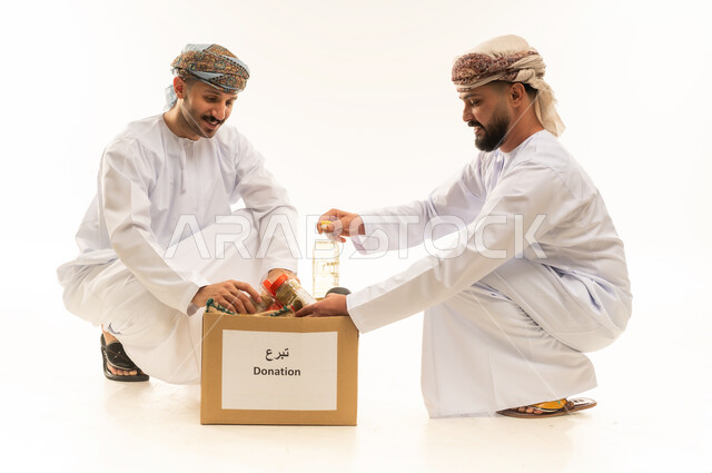 توفير المستلزمات الضرورية للفقراء، مبادرة إنسانية في سلطنة عمان، مفهوم المساعدة والتبرع، بورتريه لرجلين عربيين خليجيين عمانيين يرتديان الدشداشة والعمامة يقومان بتجهيز صناديق التبرعات، تقديم المعونة للمحتاجين، التقرب إلى الله بالعطاء والصدقة، خلفية بيضاء