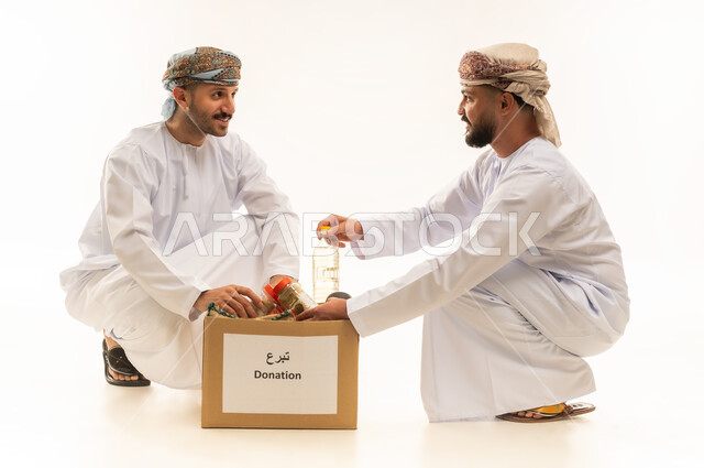 توفير المستلزمات الضرورية للفقراء، مبادرة إنسانية في سلطنة عمان، مفهوم المساعدة والتبرع، بورتريه لرجلين عربيين خليجيين عمانيين يرتديان الدشداشة والعمامة يقومان بتجهيز صناديق التبرعات، تقديم المعونة للمحتاجين، التقرب إلى الله بالعطاء والصدقة، خلفية بيضاء