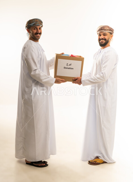 تقديم المعونة للمحتاجين، توفير المستلزمات الضرورية للفقراء، مبادرة إنسانية في سلطنة عمان، مفهوم المساعدة والتبرع والصدقة، بورتريه لرجلين عربيين خليجيين عمانيين يرتديان الدشداشة والعمامة يقومان بتجهيز صناديق التبرعات، الجسم بالطول الكامل، خلفية بيضاء