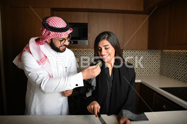 زوجان عربيان خليجيان سعوديان يساعدان بعضهم في اعداد وتجهيز الطعام ، تقطيع الخضراوات لاعداد السلطة الشهية ، تحضير وجبة صحية