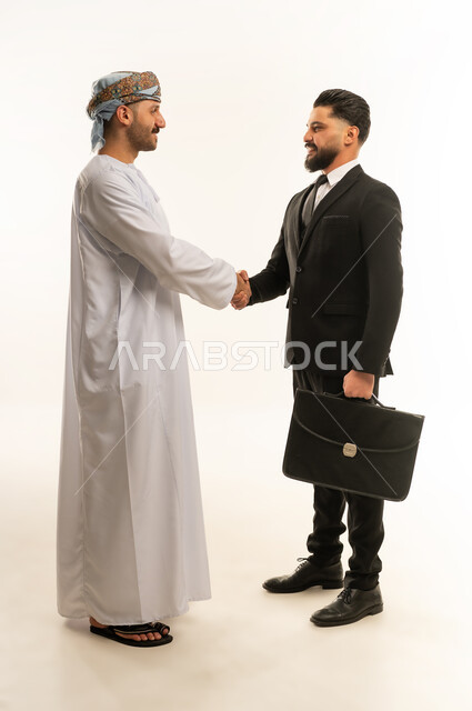 الترحيب والسلام والاستقبال، استضافة رجال الاعمال الاجانب في سلطنة عمان, تبادل الخبرات والمعرفة بين البلاد, بورتريه لرجل عربي خليجي عماني يرتدي الدشداشة والعمامة يصافح سائح اجبني يرتدي البدلة الرسمية بتعابير السرور, صورة لكامل الجسم، خلفية بيضاء