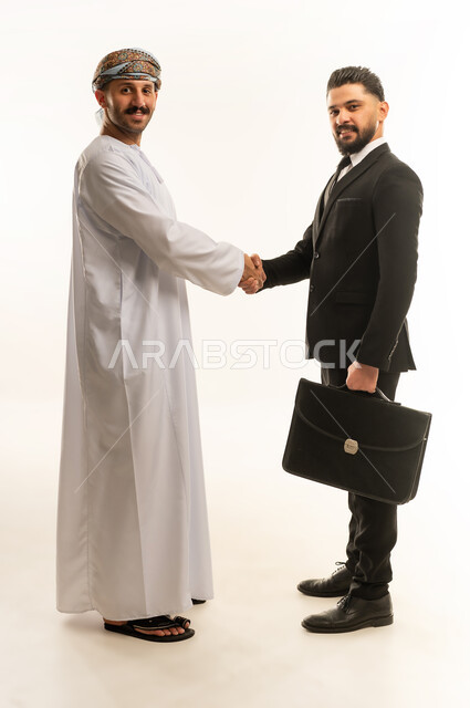 الترحيب والسلام والاستقبال، استضافة رجال الاعمال الاجانب في سلطنة عمان, تبادل الخبرات والمعرفة بين البلاد, بورتريه لرجل عربي خليجي عماني يرتدي الدشداشة والعمامة يصافح سائح اجبني يرتدي البدلة الرسمية بتعابير السرور, صورة لكامل الجسم، خلفية بيضاء