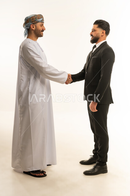 الترحيب والسلام والاستقبال، استضافة رجال الاعمال الاجانب في سلطنة عمان, تبادل الخبرات والمعرفة بين البلاد, بورتريه لرجل عربي خليجي عماني يرتدي الدشداشة والعمامة يصافح سائح اجبني يرتدي البدلة الرسمية بتعابير السرور, صورة لكامل الجسم، خلفية بيضاء