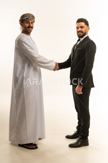 الترحيب والسلام والاستقبال، استضافة رجال الاعمال الاجانب في سلطنة عمان, تبادل الخبرات والمعرفة بين البلاد, بورتريه لرجل عربي خليجي عماني يرتدي الدشداشة والعمامة يصافح سائح اجبني يرتدي البدلة الرسمية بتعابير السرور, صورة لكامل الجسم، خلفية بيضاء