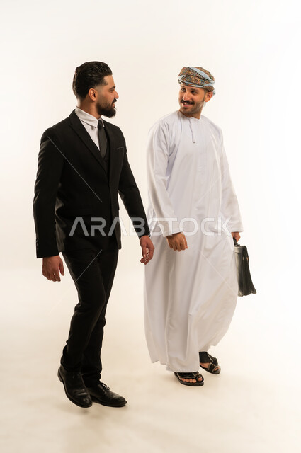 المشي والذهاب الى مكان ما، تبادل الخبرات والمعرفة بين البلاد, استضافة رجال الاعمال الاجانب في سلطنة عمان, بورتريه لرجل عربي خليجي عماني يرتدي الدشداشة والعمامة يتحاور مع سائح اجبني يرتدي البدلة الرسمية بتعابير السرور, صورة لكامل الجسم، خلفية بيضاء