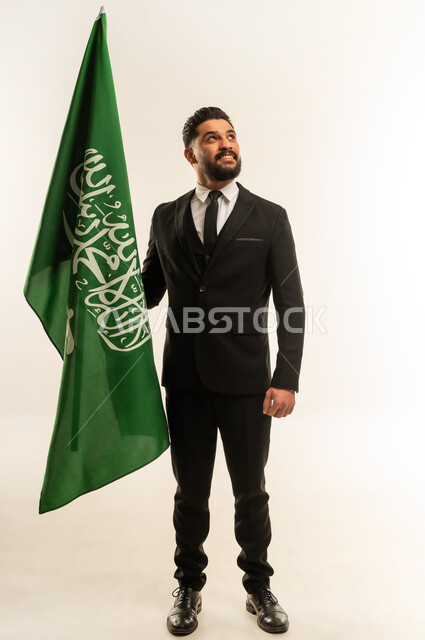 Flag Day commemoration, March 11, learning about Saudi culture and history, portrait of a smiling foreign businessman wearing a formal suit holding a flag to celebrate Saudi National Day, September 23, standing straight and firm with expressions of pride and honor, looking at the camera with gestures of pleasure, white background
