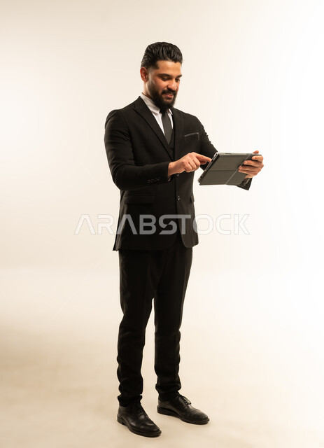 Holding a business meeting, integrating modern devices and technology into work life, browsing the internet and completing tasks remotely, following social media news, portrait of a foreign businessman in a formal suit using a tablet, full body, white background