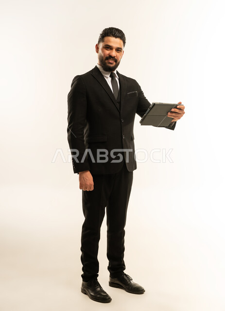 Holding a business meeting, integrating modern devices and technology into work life, browsing the internet and completing tasks remotely, following social media news, portrait of a foreign businessman in a formal suit using a tablet, full body, white background