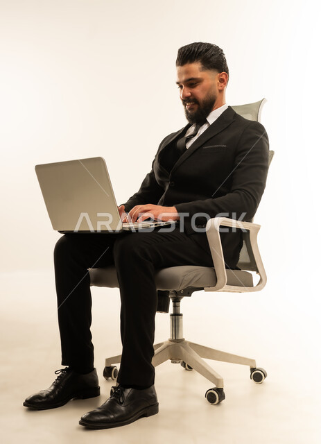 إدارة شؤون الأعمال وتنظيمها، استخدام التقنيات الحديثة المتطورة، عقد إجتماع عمل عبر الإنترنت، بورتريه لرجل اعمال اجنبي يرتدي البدلة الرسمية يجلس على الكرسي يقوم بالعمل على الحاسب المحمول, دمج التكنولوجيا في الحياة العملية، خلفية بيضاء