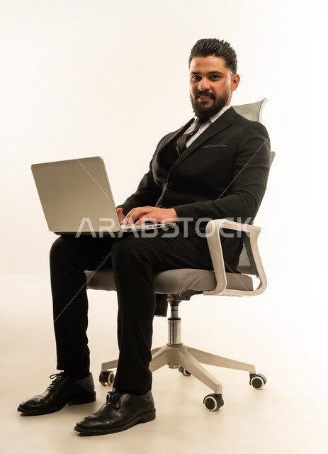 إدارة شؤون الأعمال وتنظيمها، استخدام التقنيات الحديثة المتطورة، عقد إجتماع عمل عبر الإنترنت، بورتريه لرجل اعمال اجنبي يرتدي البدلة الرسمية يجلس على الكرسي يقوم بالعمل على الحاسب المحمول, دمج التكنولوجيا في الحياة العملية، خلفية بيضاء
