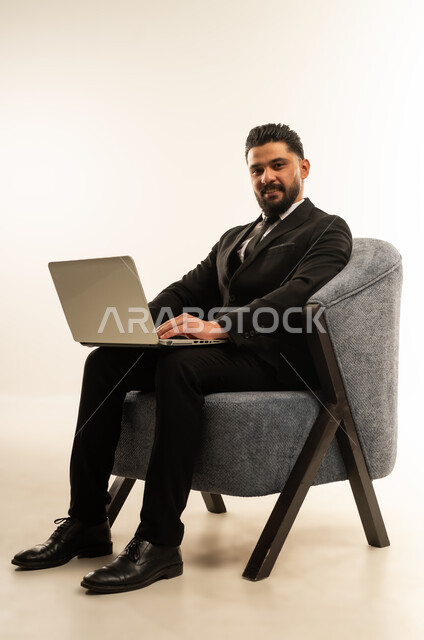 Business management and organization, use of modern advanced technologies, holding a business meeting online, portrait of a foreign businessman in a formal suit sitting on a chair working on a laptop, integrating technology into business life, white background