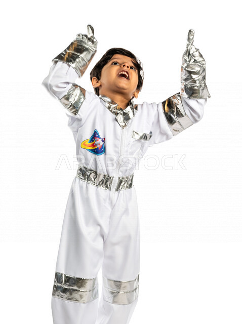 Portrait of a smiling Saudi Arabian Gulf Arab boy, wearing an astronaut costume, raising his hand up, dreaming of becoming an astronaut, pointing his index finger up with different facial and hands gestures indicating happiness, dream of reaching space an