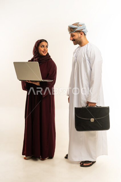 العمل الجماعي وروح الفريق الواحد، بورتريه لزميلين عربيين عمانيين خليجيين يقومان بمناقشة و تنظيم الاعمال بإستخدام جهاز الحاسوب المحمول، تبادل الأفكار والخبرات لتحقيق أهداف الشركة، دمج العمل مع التقنية والتكنولوجيا، صورة الجسم بالطول الكامل، خلفية بيضاء