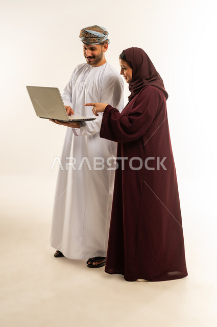 العمل الجماعي وروح الفريق الواحد، بورتريه لزميلين عربيين عمانيين خليجيين يقومان بمناقشة و تنظيم الاعمال بإستخدام جهاز الحاسوب المحمول، تبادل الأفكار والخبرات لتحقيق أهداف الشركة، دمج العمل مع التقنية والتكنولوجيا، صورة الجسم بالطول الكامل، خلفية بيضاء