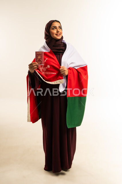 وثيقة سفر رسمية، إحياء ذكرى تأسيس الدولة 1775 م، حب الوطن والانتماء إليه، بورتريه من الخلف لإمرأة عربية خليجية عمانية ترتدي الحجاب والعباءة والعلم الوطني للبلاد تمسك جواز السفر، ذكرى اليوم الوطني العماني 18 نوفمبر، الجسم بالطول الكامل، خلفية بيضاء