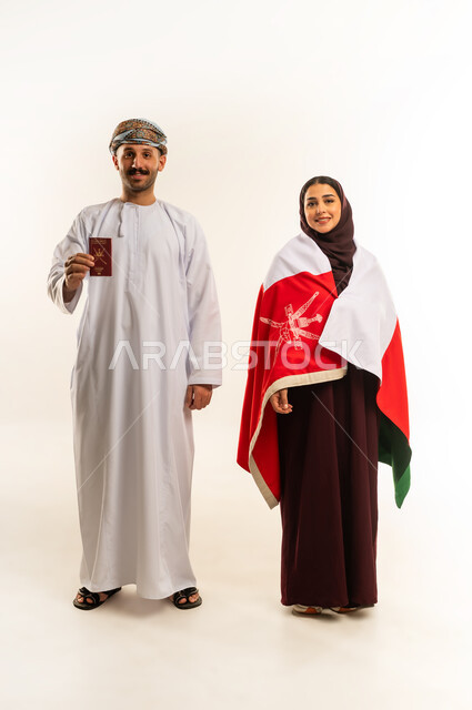 Omani National Day, November 18, commemorating the founding of the state in 1775 AD, official travel document, portrait of an Omani Gulf Arab man wearing a dishdasha and turban holding an international entry and exit visa standing next to a woman wearing a hijab and abaya, placing the country's flag on her shoulder, full body, white background