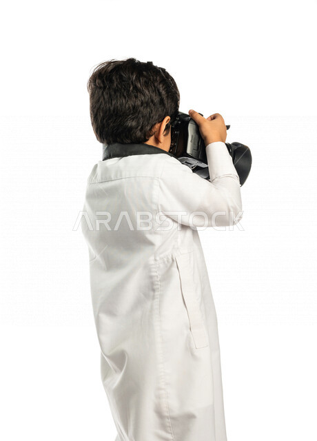 Portrait of a Saudi Arabian Gulf boy, holding a camera in his hand, taking pictures using the photography camera, photography, talent and professionalism in the art of photography, small photographer, high-resolution camera, white background