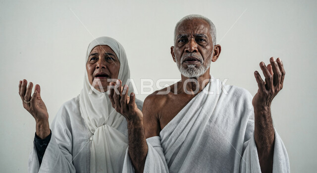 رفع اليدين والدعاء بخشوع وتضرع، مفهوم أركان الإسلام وأداء الفرائض الدينية، بورتريه مقرب لشاب حاج خليجي عربي سعودي يرتدي ثياب الإحرام يقف بجانب زوجته باستقامة بتعابير السرور، تأدية مناسك الحج والعمرة، العبادة والتقرب إلى الله، خلفية بيضاء