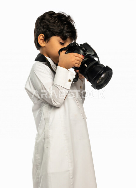 Portrait of a Saudi Arabian Gulf boy, holding a camera in his hand, taking pictures using the photography camera, photography, talent and professionalism in the art of photography, small photographer, high-resolution camera, white background