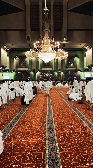 مجموعة من الحجاج المسلمين يرتدون لباس الإحرام يؤدون الصلاة في مسجد السيدة عائشة في ميقات التنعيم، الإستعداد لأداء فريضة الحج في مكة المكرمة، العبادة والتقرب إلى الله، الديكور الداخلي للمساجد في المملكة العربية السعودية
